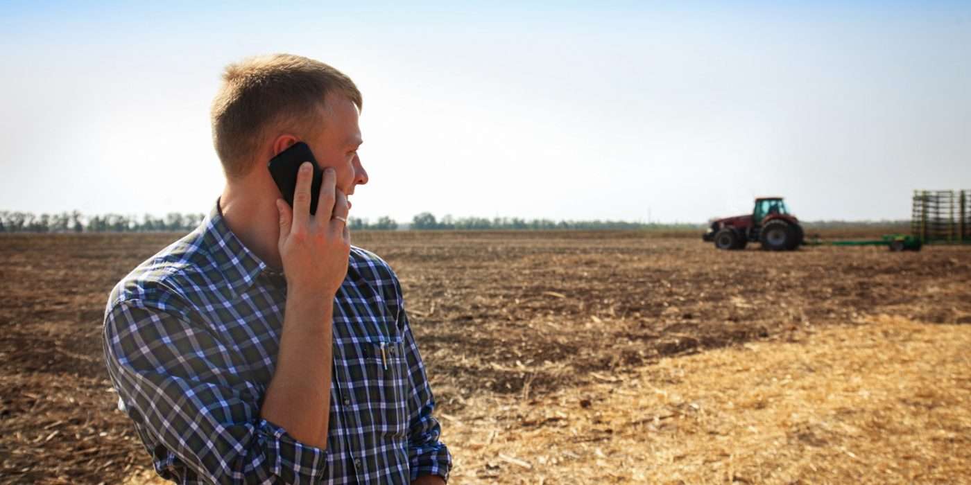 man on phone looking behind to tractor in dusty field